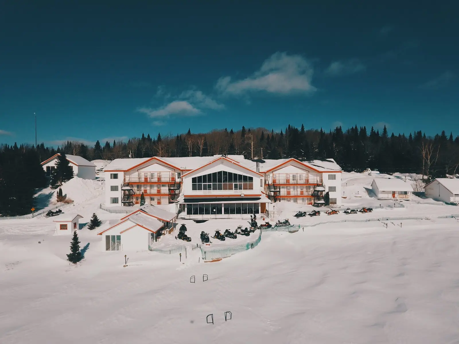 Lodge of Pourvoirie Au Pays de Réal Massé in Lanaudière surrounded by snow with snowmobiles parked in front of the main building.