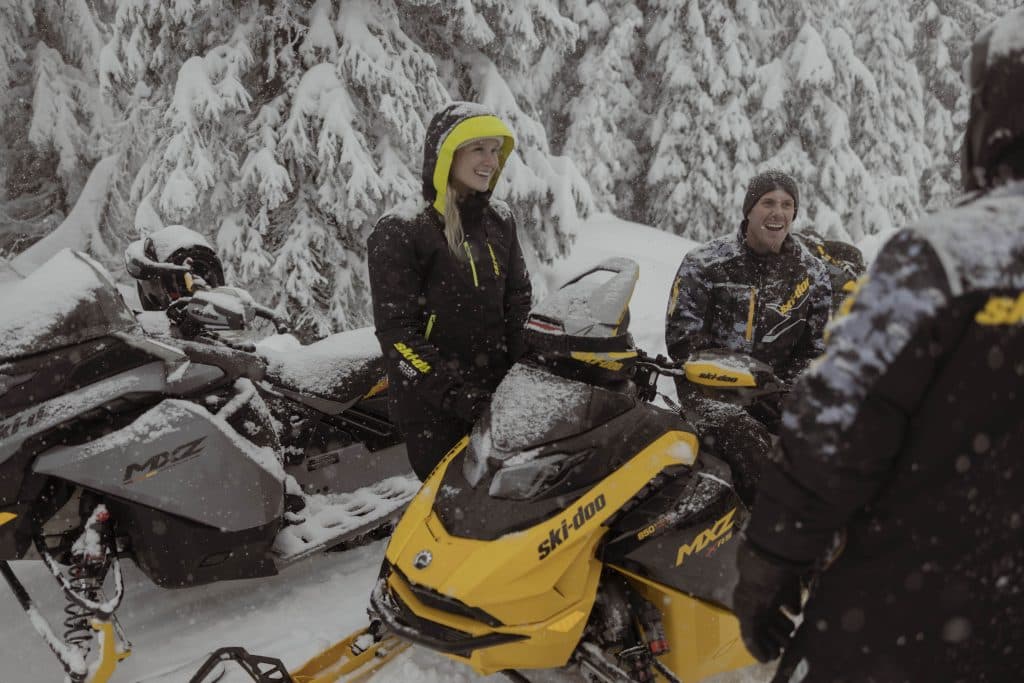 three people sitting on their ski-doo 2025 snowmobile in a circle discuss