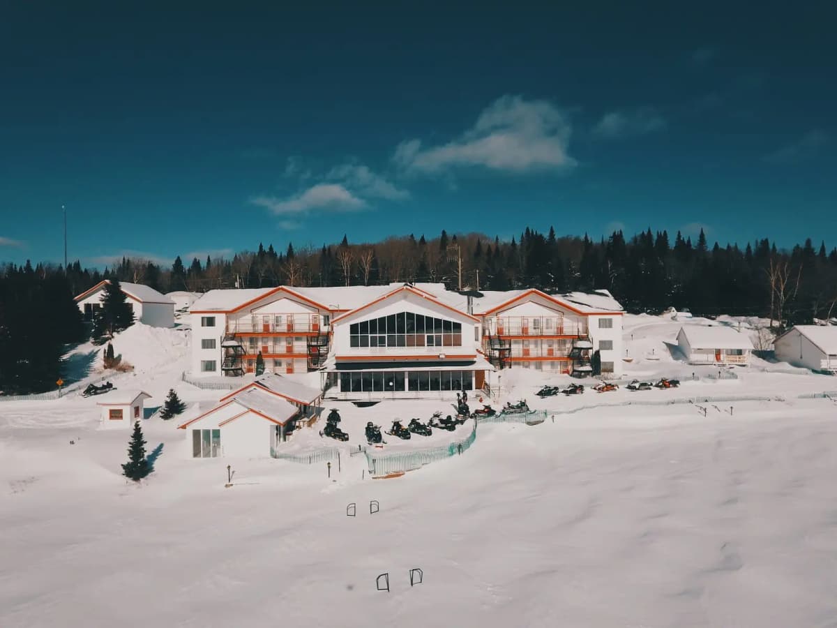 Lodge of Pourvoirie Au Pays de Réal Massé in Lanaudière surrounded by snow with snowmobiles parked in front of the main building.