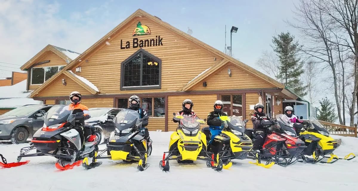 Snowmobilers in front of the wooden building at La Bannik, lined up with their colourful snowmobiles.