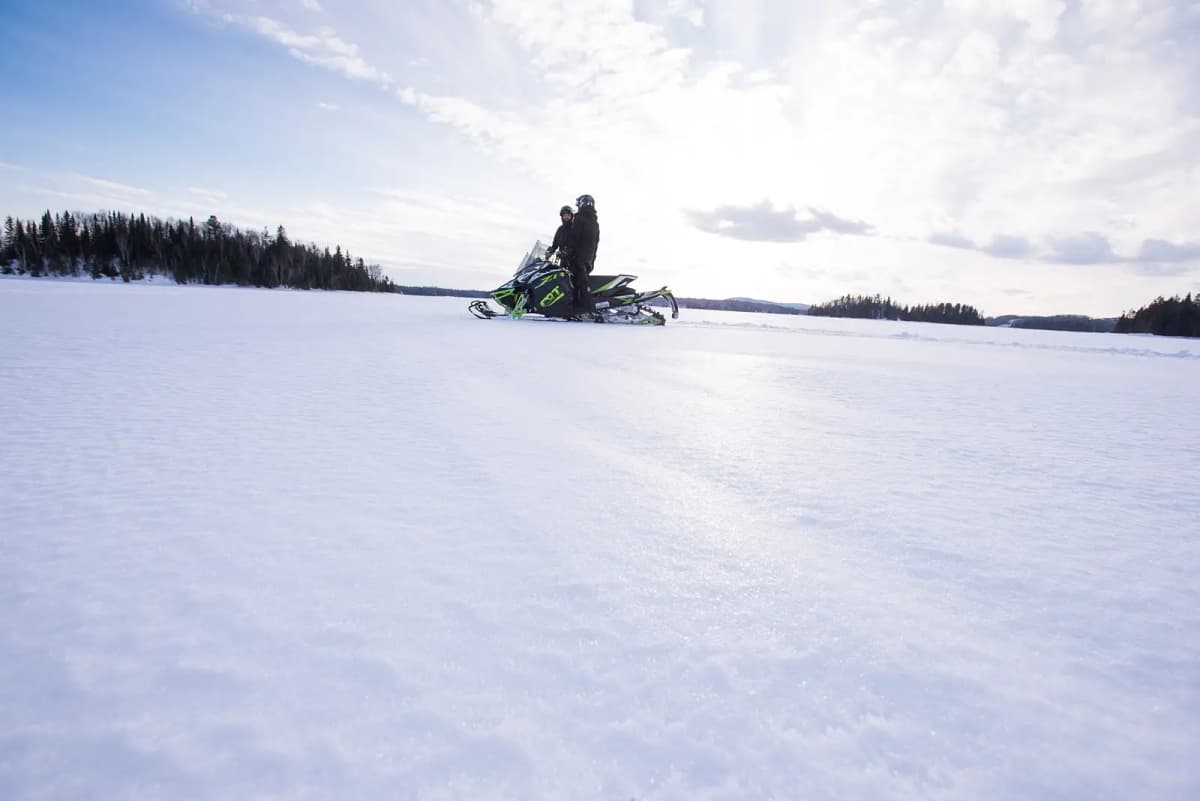 Two snowmobilers crossing a frozen lake in Abitibi-Témiscamingue on snow-covered trails.