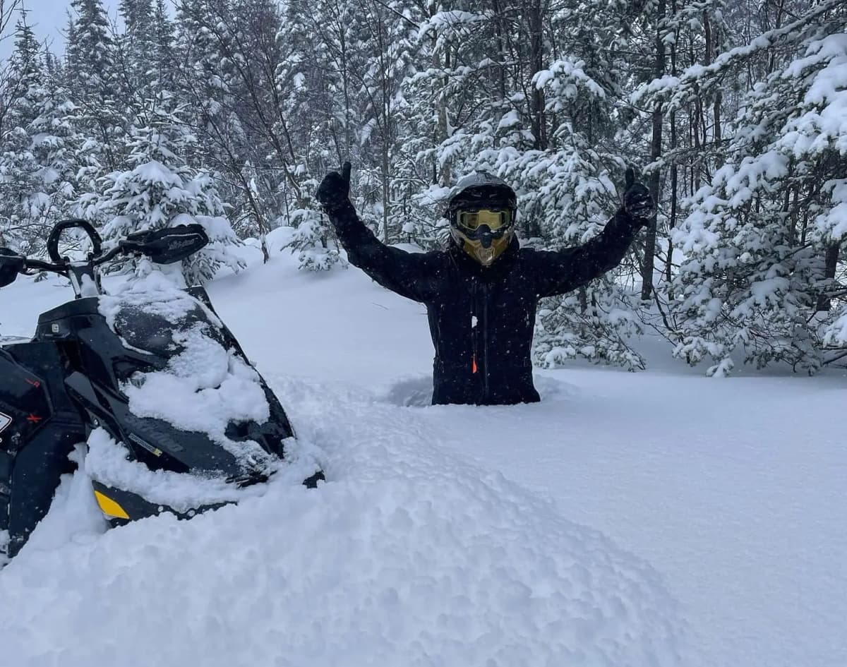 Andrew Ranger in the snow up to his hips next to his backcountry snowmobile